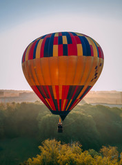 Fototapeta premium Colorful hot air balloon takes off from green park in small european city at summer sunrise