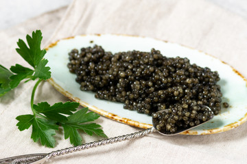 Black caviar. Black sturgeon caviar in a ceramic bowl and a metal spoon on a light background. Useful delicacy