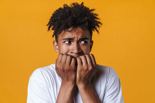 Image of scared african american guy biting his fingernails