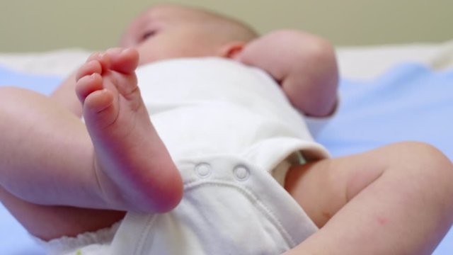 Close up shot of adorable newborn baby in bodysuit and diaper lying on back and sucking pacifier