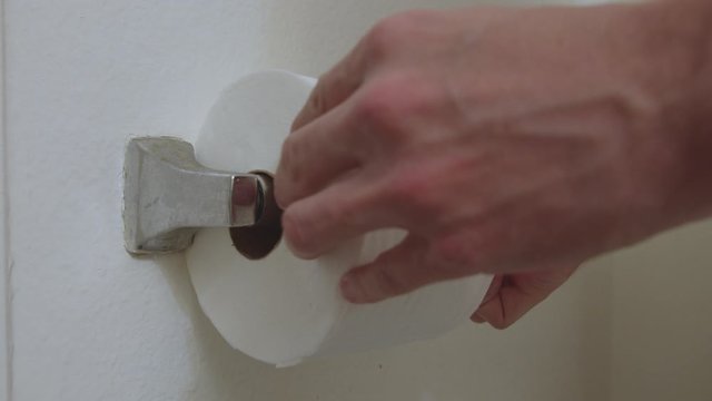 Males hands changing empty toilet paper roll, in a restroom with a new one from a side angle