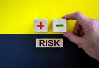 Businessman holds a cubes with minus icon. Wooden cubes with  word 'risk'. Beautiful yellow and black background. Copy space. Business concept.