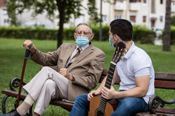 Grandfather and grandson spending quality time in park talking and playing guitar with covid masks