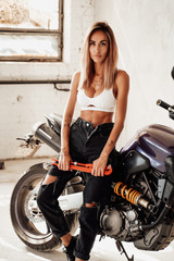 A blond girl is staying with sport bike behind in white garage
