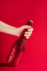 Modern design template with female hand holding champaigne bottle covered in red sequines on red background. Christmas background concept. Holiday celebration concept. Modern template for your design.