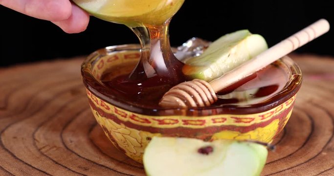 Dips an apple into honey in a bowl on a wooden stand, Rosh hashanah - jewish New Year holiday concept.
