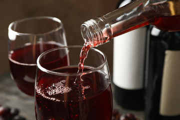 Wine is poured from a bottle in glass on wooden table, close up