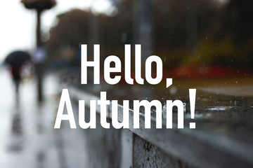 Raindrops fall on the parapet on the city sidewalk. Man with an umbrella in blur. Hello autumn text
