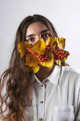 A woman wearing a protective mask during quarantine and pandemic. Mask of leaves and berries of rowan viburnum. Autumn concept. Health care.