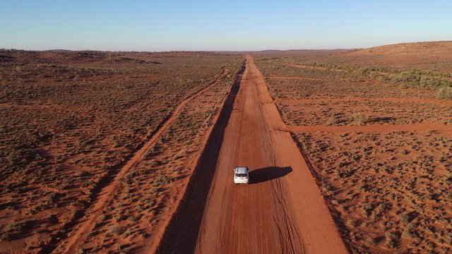 Aerial: Drone shot tracking closely behind a vehicle driving down an empty road in the Australian outback towards the horizon near Broken Hill, Australia