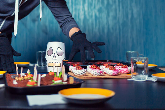 A woman in a robber's costume steals sweets from a holiday table. Hands and food close up. The concept of Halloween