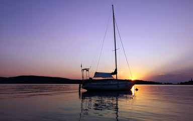 A sailboat anchored in a bay  on sunset