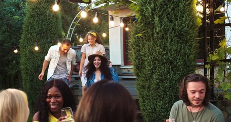 Many mixed races young cheerful males and females gathering together and having fun at garden. African American girl laughing in good mood. Caucasian joyful beautiful girls hugging. Friendship concept