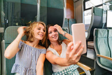 Two smiling girlfriends in train taking selfies