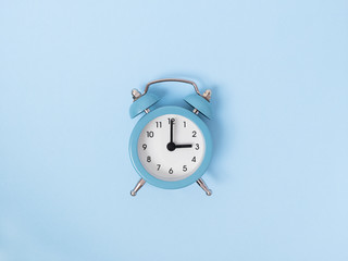 Retro alarm clock middle of blue background. Monochrome simple flat lay with pastel texture. Time concept. Stock photo.