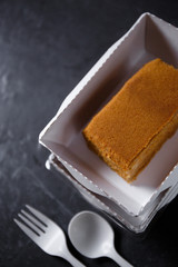 
Big rusk of honey cake in a disposable paper box with disposable cutlery on a dark background