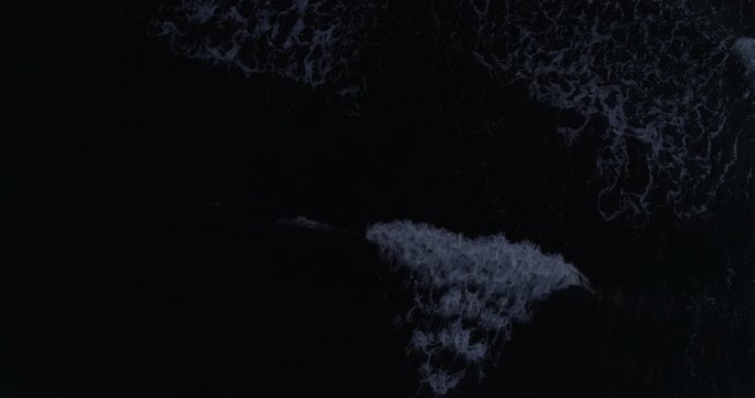 Overhead drone shot ascending over waves breaking on a beach at night