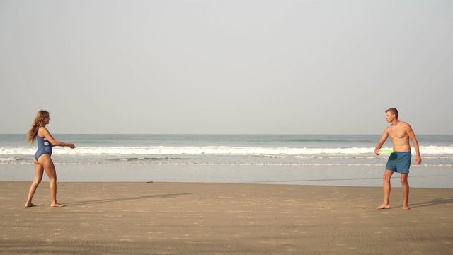 Young beautiful couple man and woman playing with a flying disc on the sea beach