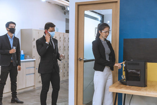 Business People Wearing Face Mask Stand In Line With Physical Distancing During Waiting For Use Coffee Machine At Office. New Normal Life.