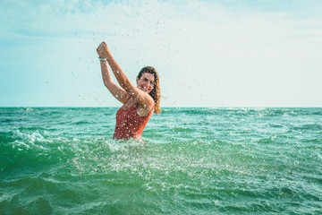 Beautiful young European woman with an orange swimsuit splashing water at the sea in Cádiz