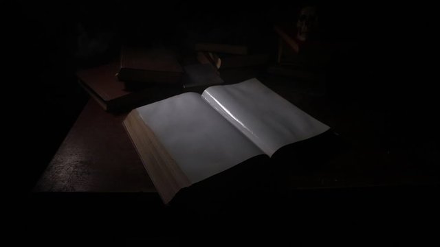 A stack of old books. Vintage book on wooden table. Magic lightning around a glowing book in the room of darkness. Selective focus