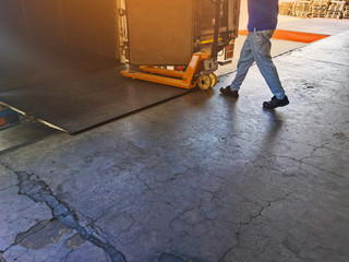 Worker driving forklift loading shipment carton boxes and goods on wooden pallet at loading dock from container truck to warehouse cargo storage in freight logistics and transportation industrial