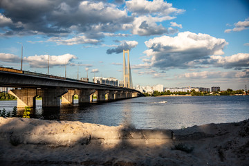 South bridge in Kyiv Ukraine. Bottom view from the right sandy bank of the bridge, the Dnieper and the left bank. Sunny day and sky with clouds. Horizontal orientation. High quality photo
