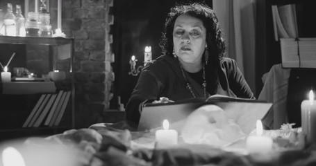 Old serious witch reading magical book in her office