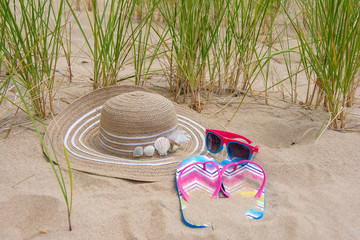 woman's stylish summer hat decorated with seashells in beach sand with sunglasses and flip-flops