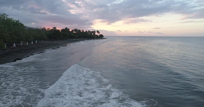 Drone crane shot from waves breaking on a black sandy beach to reveal beautiful sunset over landscape