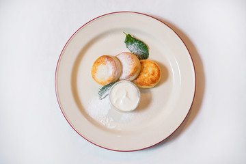 Curd pancakes with sour cream garnished with powdered sugar and mint. The concept of a delicious hearty homemade breakfast served in a restaurant.