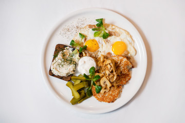Potato pancakes with mushrooms and fried eggs, served with bread and pickled cucumbers. The concept of a delicious hearty homemade breakfast served in a restaurant.