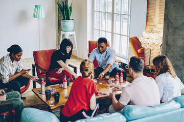 Diverse hipster guys playing cards at table with chips for poker during drinks friendly meeting, casual dressed multicultural youngsters spending free time for together gaming and recreating