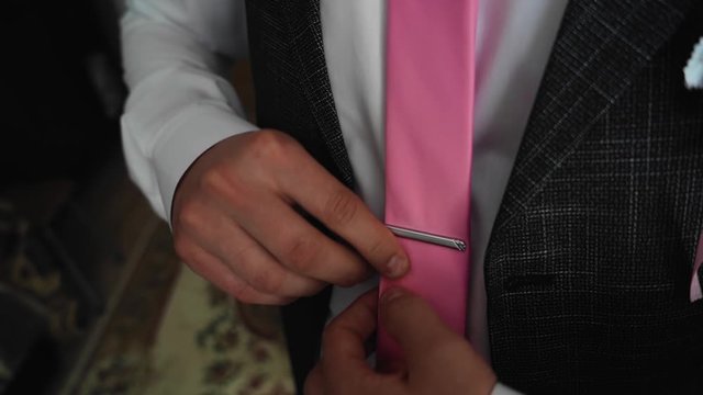 The guy puts on a pink tie and pin it to his shirt.