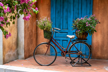 Fototapeta na wymiar Vintage bike with basket full of flowers next to an old building in Danang, Vietnam, close up