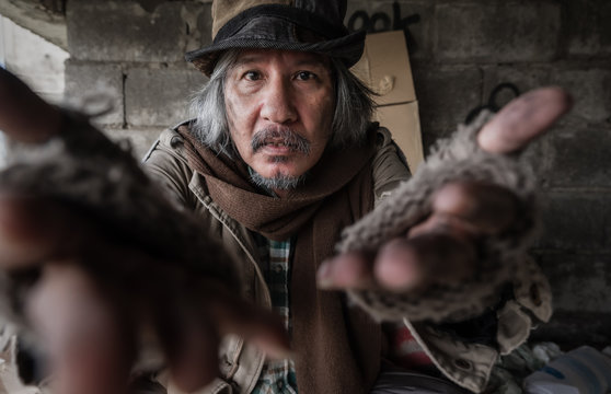 Old homeless man with gray beard wear gloves with sitting and hands up for asking help and food beggar because hungry. Closeup and focus to dirty face of poor man beggar. Help and hope concept.
