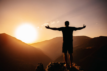 man silhouette  is standing with open arms in front of  mountains on sunset, feeling free