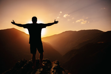 man silhouette  is standing with open arms in front of  mountains on sunset, feeling free