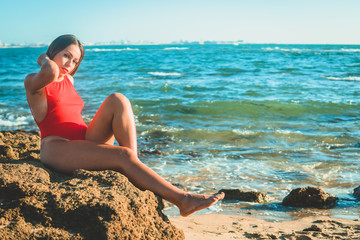 Fototapeta na wymiar young woman in a red swimsuit on the beach sitting on a rock