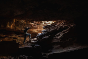 Woman backpacker walking in cave with sunlight.
