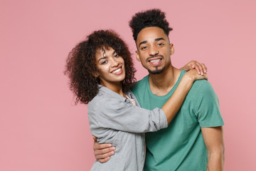 Smiling cheerful funny young african american couple two friends guy girl in gray green casual clothes posing hugging looking camera isolated on pastel pink color wall background studio portrait.