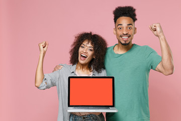 Joyful african american couple friends guy girl in gray green clothes hold laptop computer with blank empty screen mock up copy space doing winner gesture isolated on pink background studio portrait.