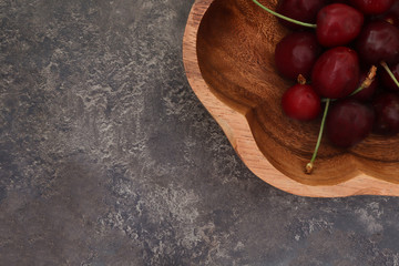 A heap and a large wooden bowl of fresh red ripe cherries whit free space fpr text.