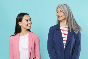 Smiling beautiful two asian female business women employer and employee in pink blue jackets posing working in office looking at each other isolated on pastel blue color background studio portrait.