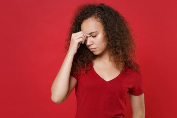 Tired young african american girl in casual t-shirt posing isolated on red wall background studio portrait. People emotions lifestyle concept. Mock up copy space. Put hand on nose keeping eyes closed.
