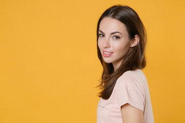Obraz premium Side view of smiling beautiful attractive young brunette woman 20s wearing pastel pink casual t-shirt standing posing looking camera isolated on bright yellow color wall background studio portrait.
