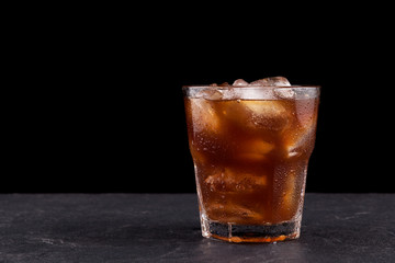 Iced coffee with ice in a transparent misted glass against a dark background with copy space. Close-up, selective focus