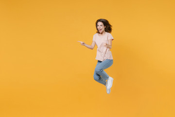 Fototapeta na wymiar Full length portrait of excited cheerful young brunette woman 20s wearing pastel pink casual t-shirt posing jumping pointing index fingers aside isolated on bright yellow color wall background studio.