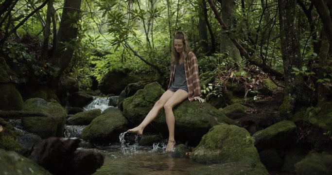 Cute girl sitting on a mossy rock playing in the water on a mountain stream