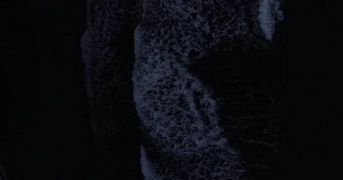 Overhead drone shot at dusk over waves breaking on a black sandy beach